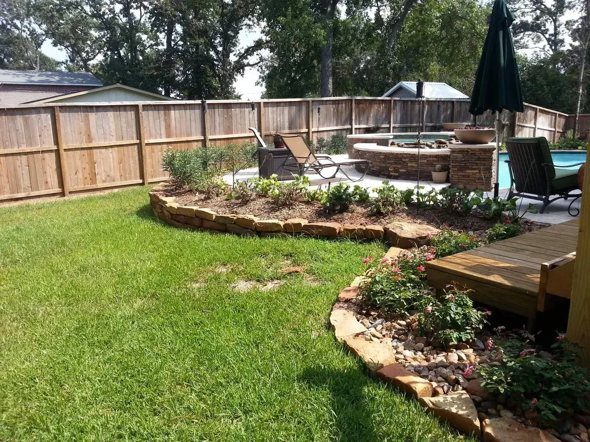 Backyard with fire pit, pool, and wooden fence surrounded by landscaping and lawn.