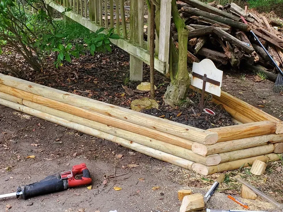 Raised garden bed made of stacked logs with a reciprocating saw in the foreground.