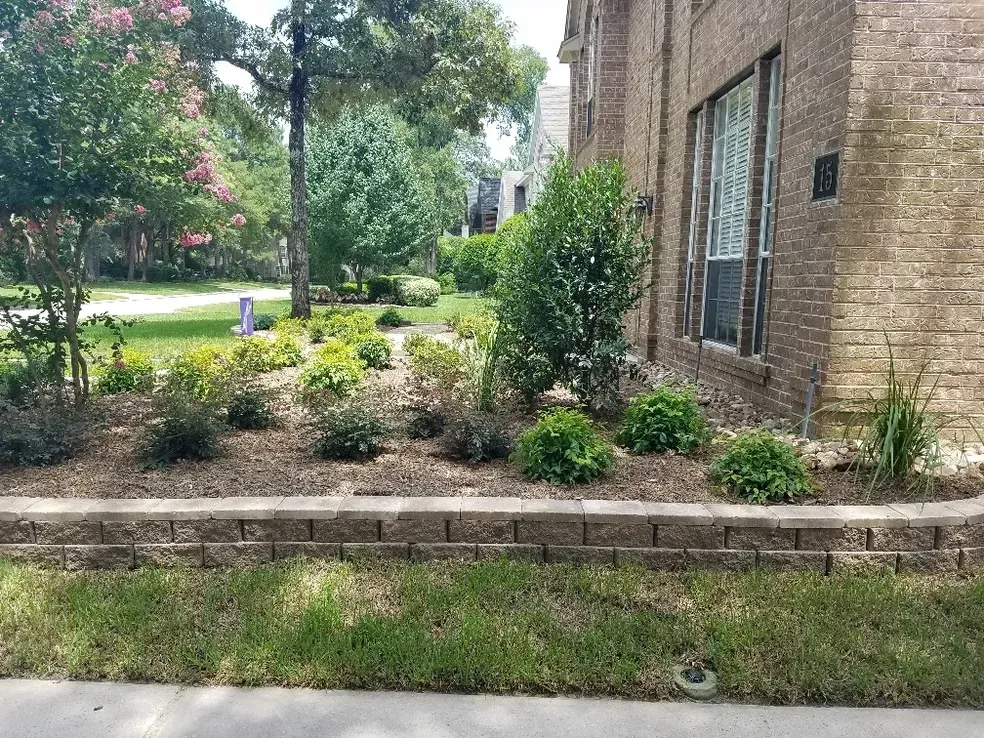 Brick wall with landscaped flowerbeds and green grass.