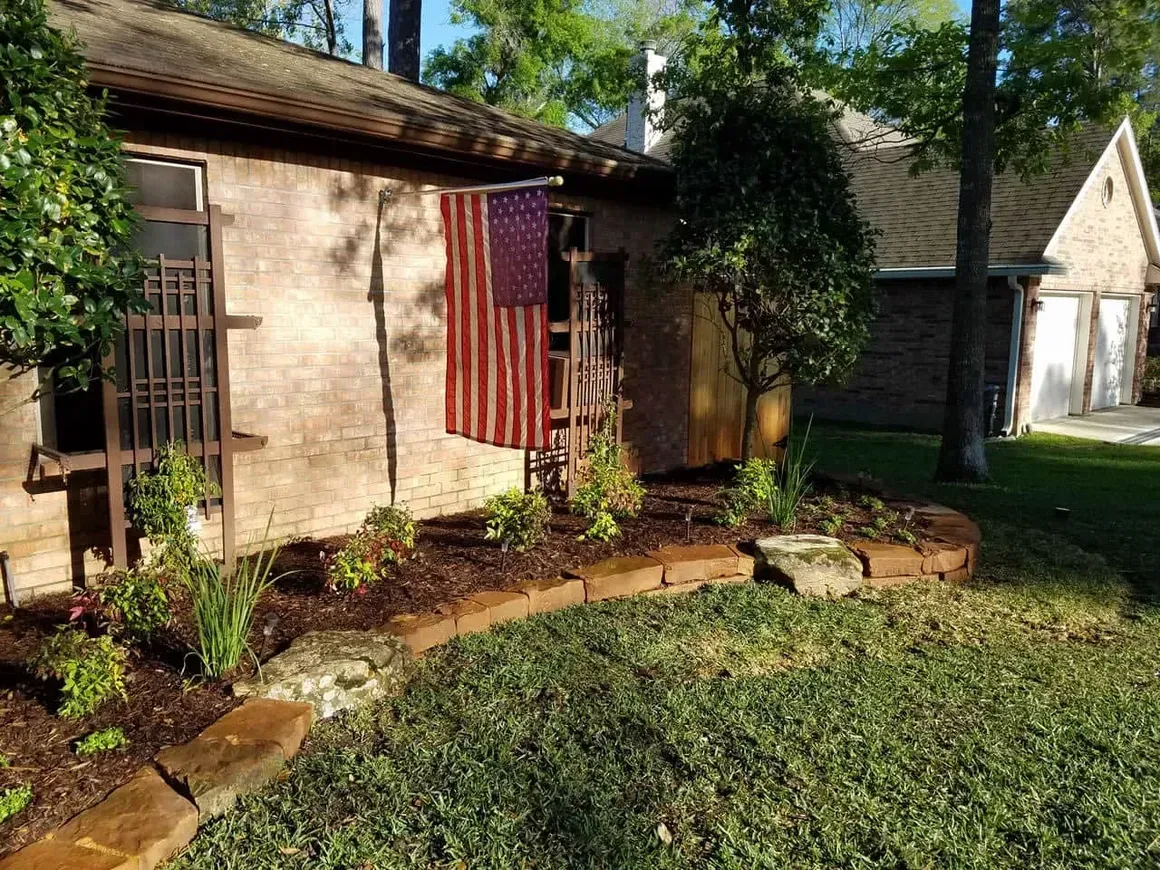 A house with an American flag, flower bed, and green grass.