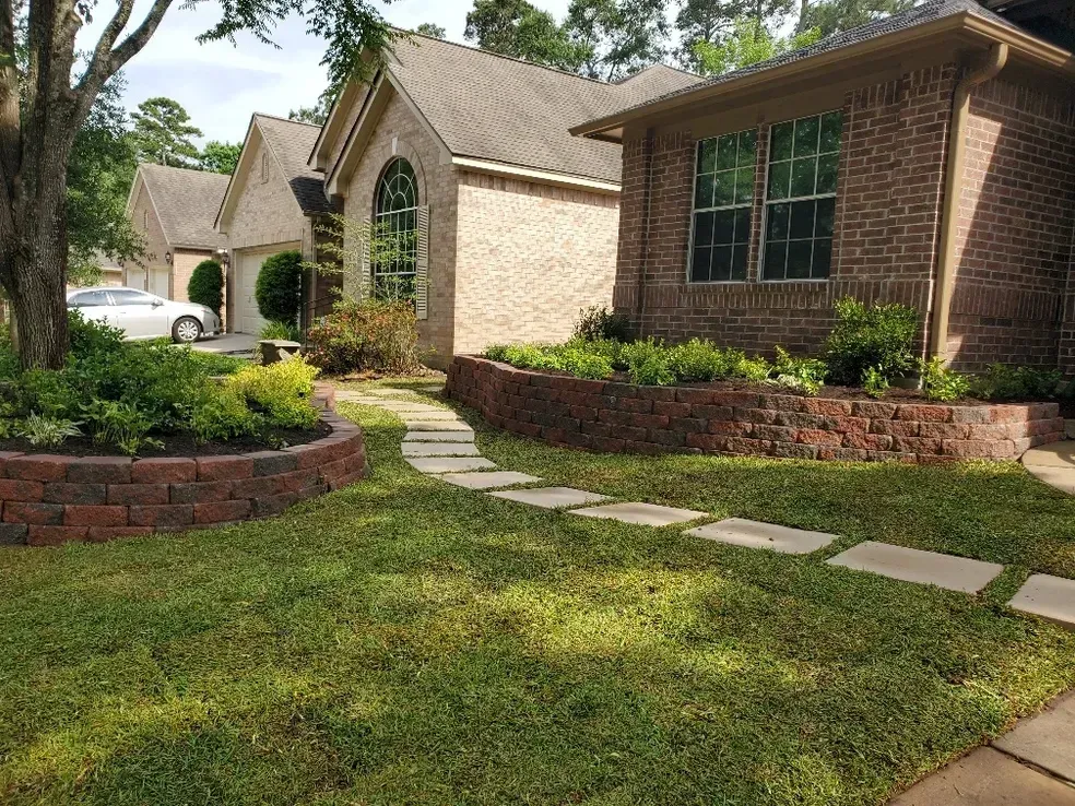 Brick houses with well-maintained landscaping, including raised flower beds and a stone path.