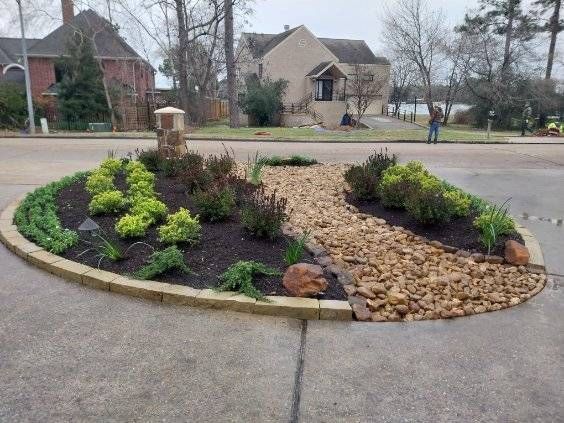 Oval-shaped landscaped median with stone path and small plants, brown and green. Houses and person visible in background.