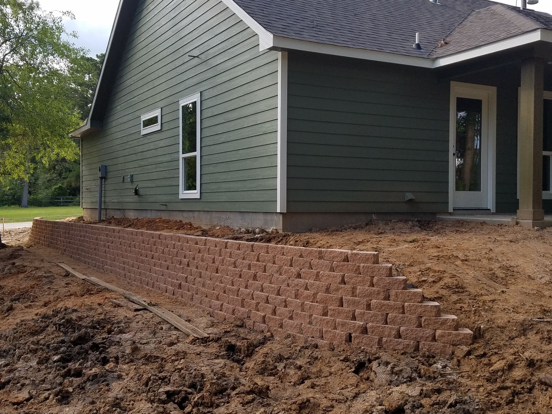 Retaining wall of brown blocks in front of a green-sided house with white trim.
