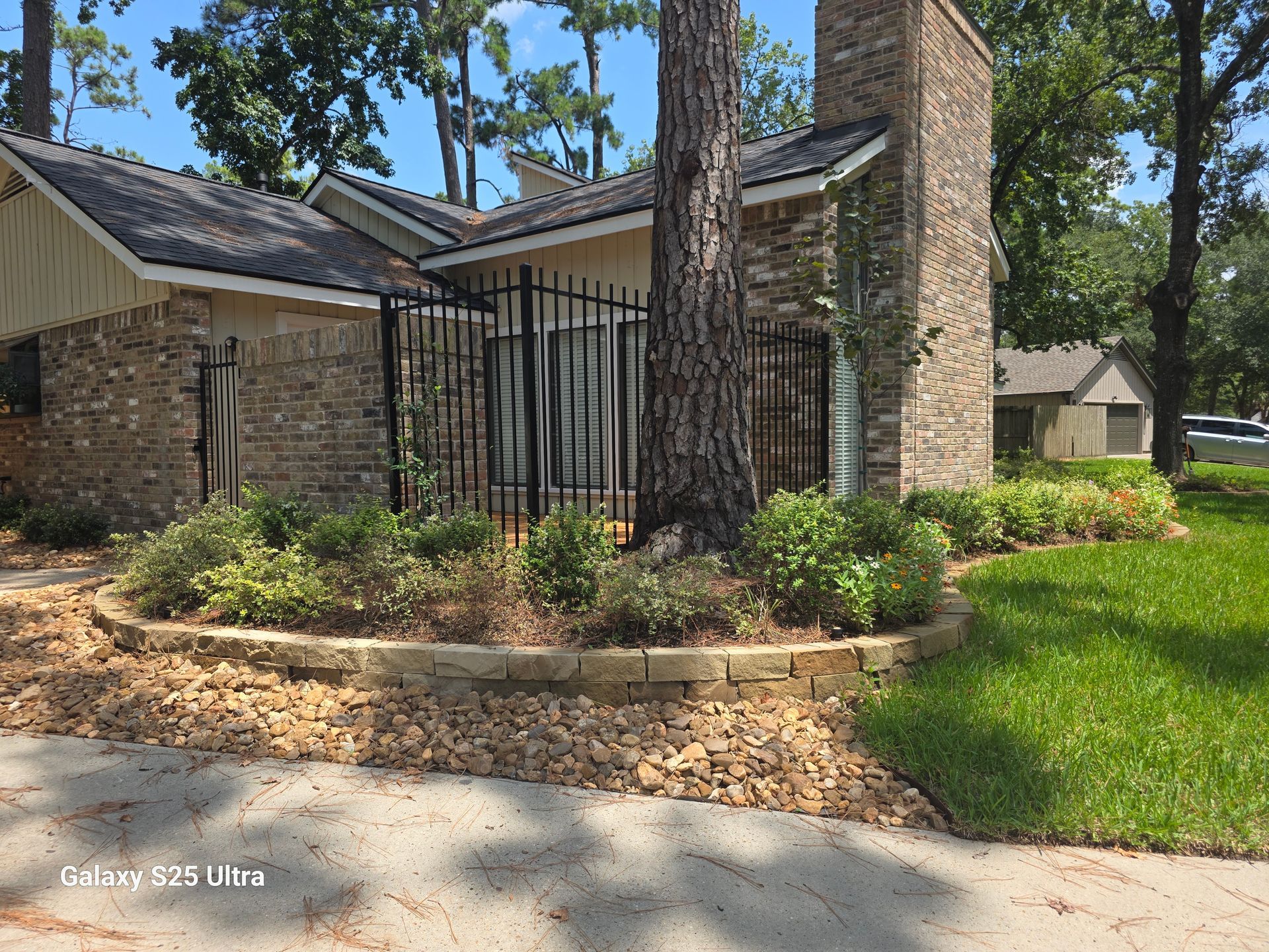 Building with brick exterior, black fence, and tree in a landscaped yard.