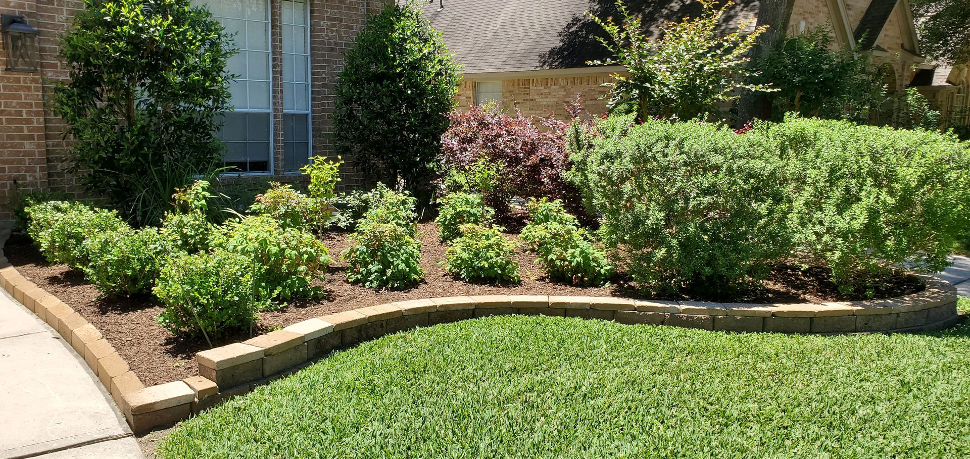 Landscaped front yard with green lawn, shrubs, and brick border.