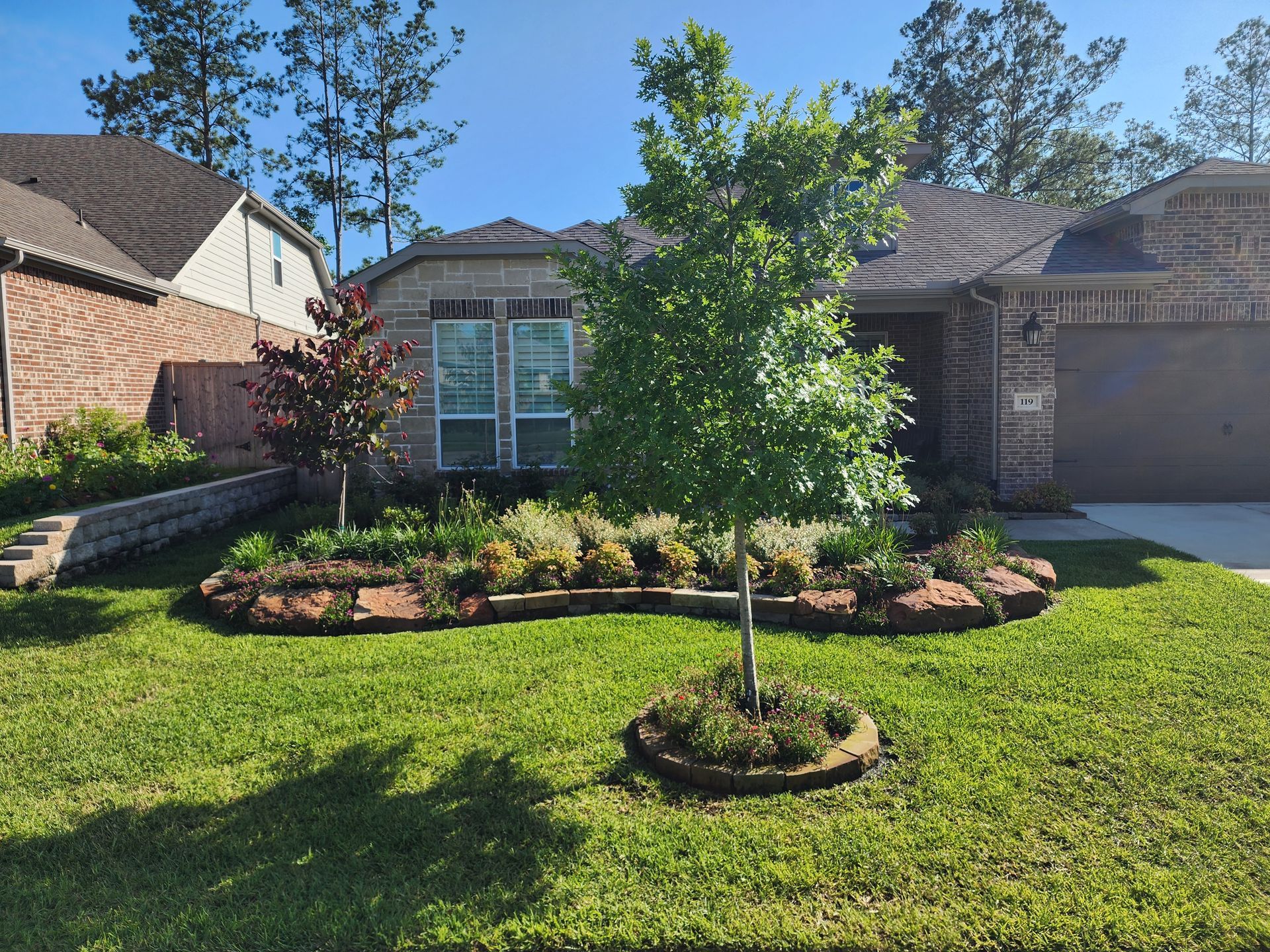 Well-manicured front yard with landscaping beds, a tree, and a single-story house.