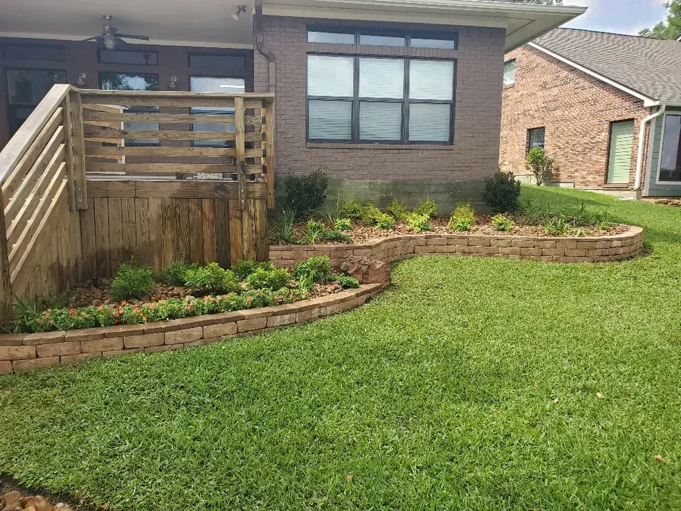 Backyard with a brick retaining wall and a wooden deck, grass lawn.