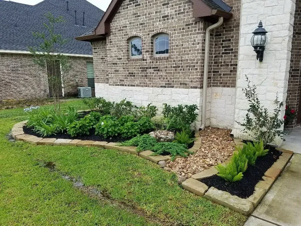 A house with a brick facade and landscaping, including a flower bed and a lawn.