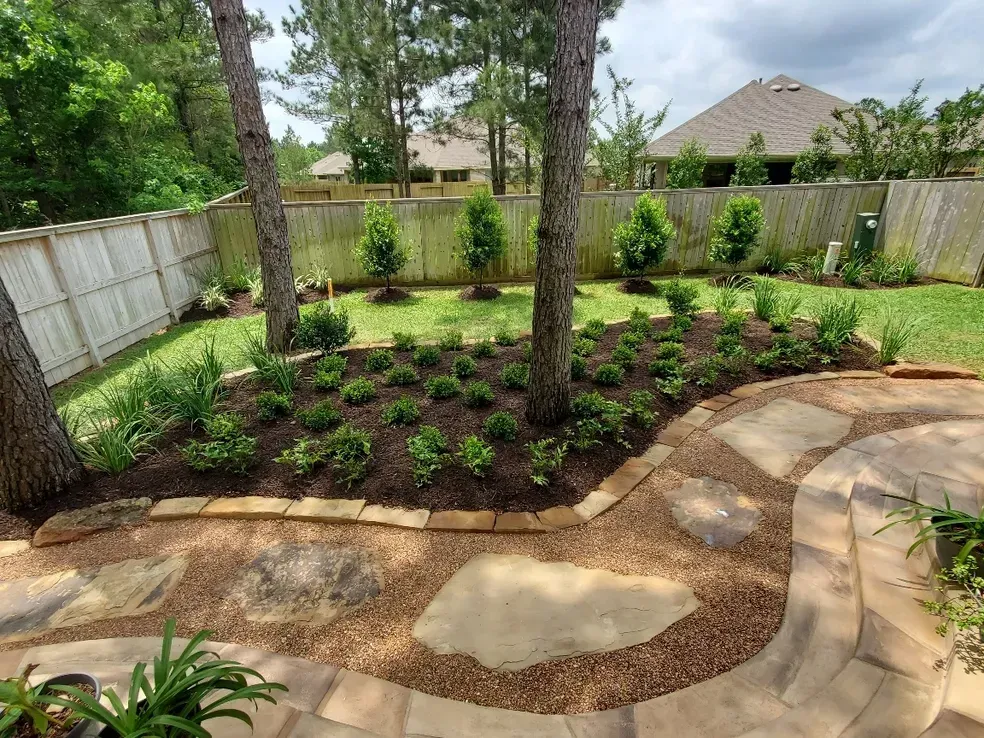 Backyard garden with flagstone path, flower beds, trees, and wooden fence.