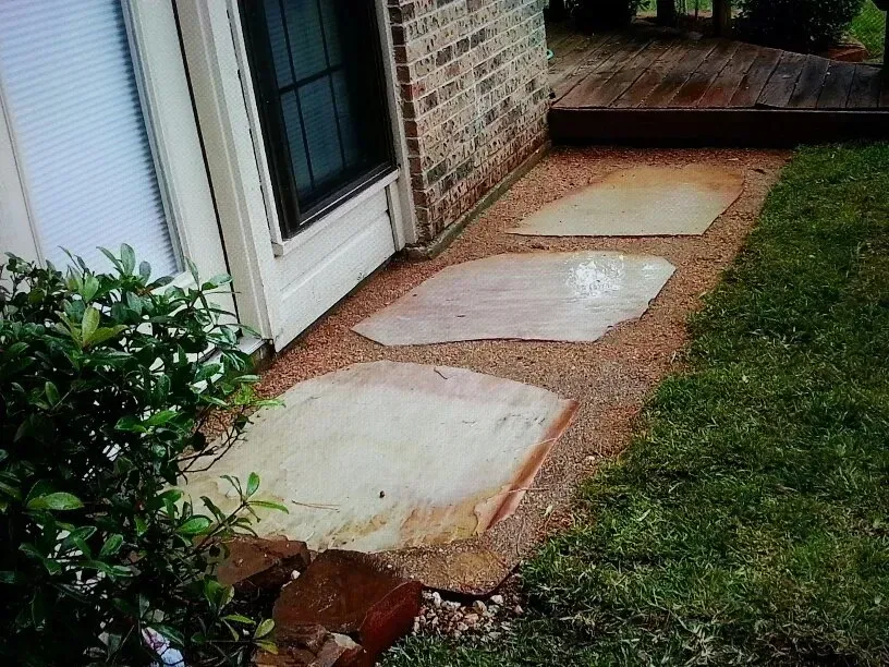 Stone pavers set in gravel path next to a building and lawn.
