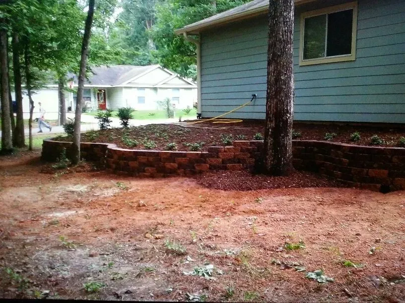 Brick retaining wall with newly planted landscaping near a house.