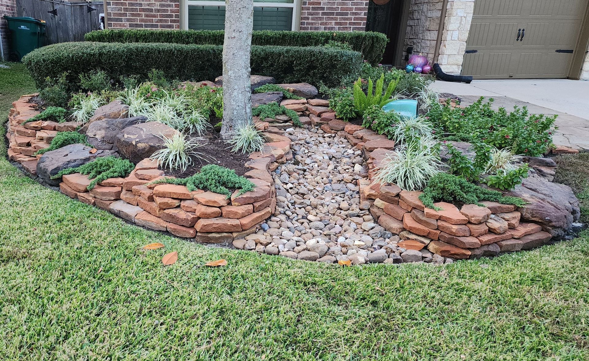 Landscaped front yard with brick border, rock creek bed, and various plants. Green grass surrounds.