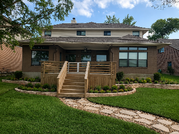 Brick retaining wall in front of a green-sided house, built on a slope of dirt.