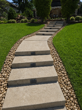 Stepping stone walkway through a landscaped garden, bordered by small rocks and green grass