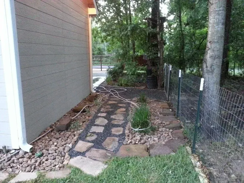 Stone path next to a building, along a fence. Rocks and plants border the path.