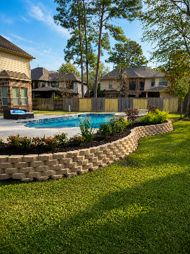 Backyard pool with stone border, green lawn, and suburban houses under trees