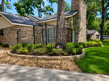 Brick retaining wall with flower bed in front of a house, pathway leads to the left.