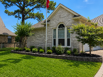 Single-story brick house with arched window, green lawn, and landscaped front yard under a blue sky
