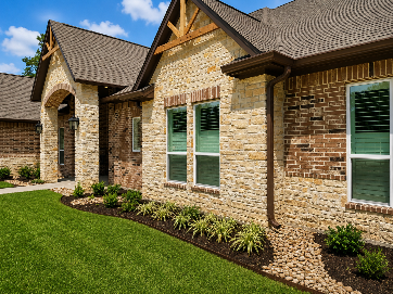 Brick house exterior with green shutters, arched entry, and landscaped lawn under blue sky