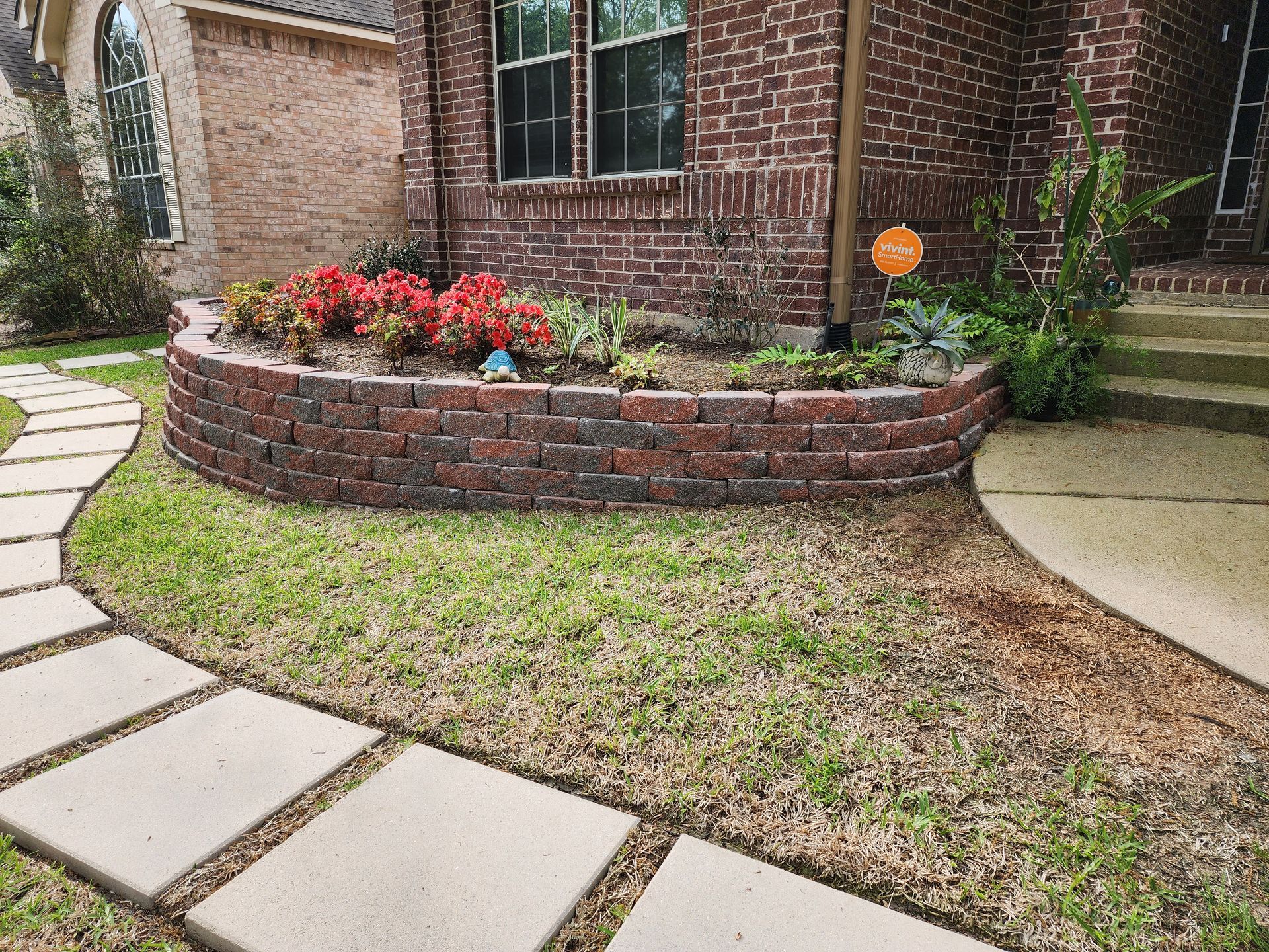 Brick retaining wall with flower bed and stepping stone path in front of a brick house.