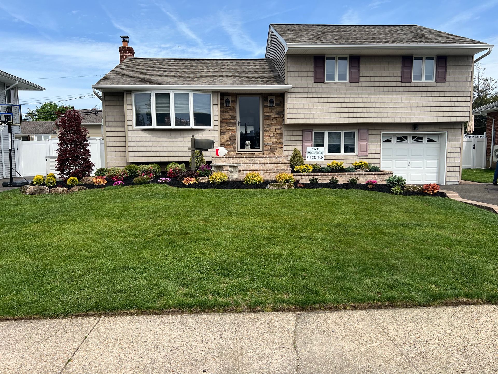 A two-story, split-level suburban house with light siding, a brick entryway, a garage, and a manicured front lawn.
