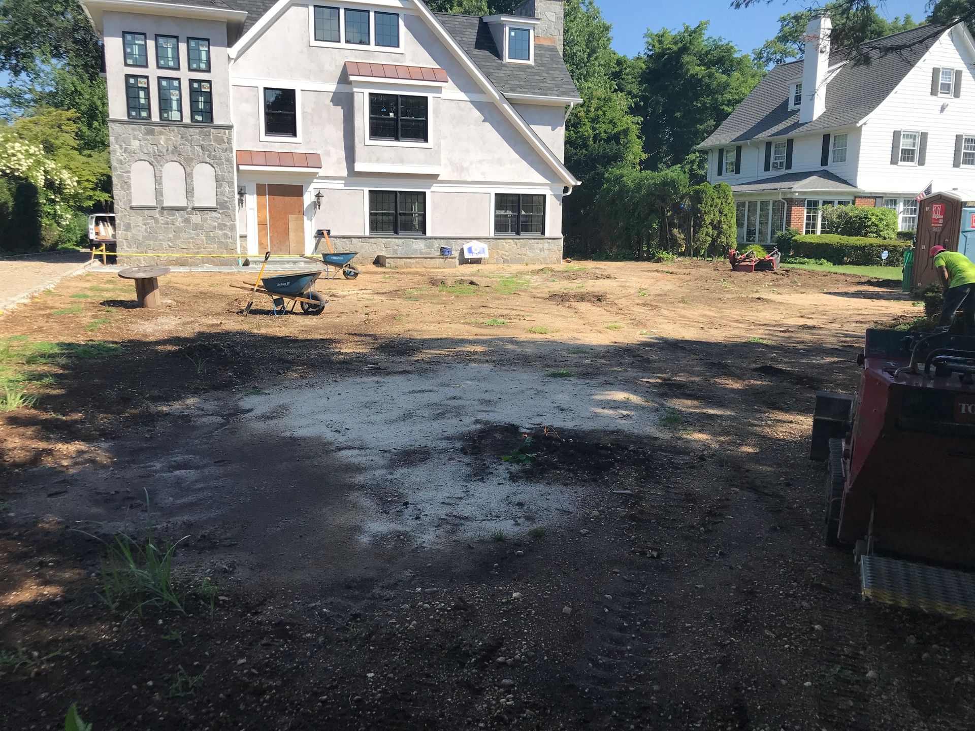 A house under construction with a large, dirt-covered yard, wheelbarrows, and machinery in the foreground.