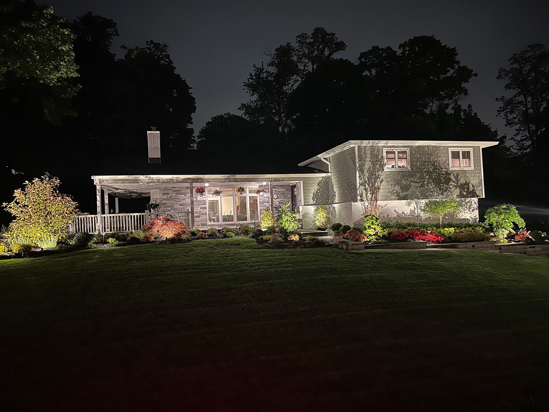 A split-level home illuminated by landscape lighting at night, surrounded by trees and landscaped gardens.