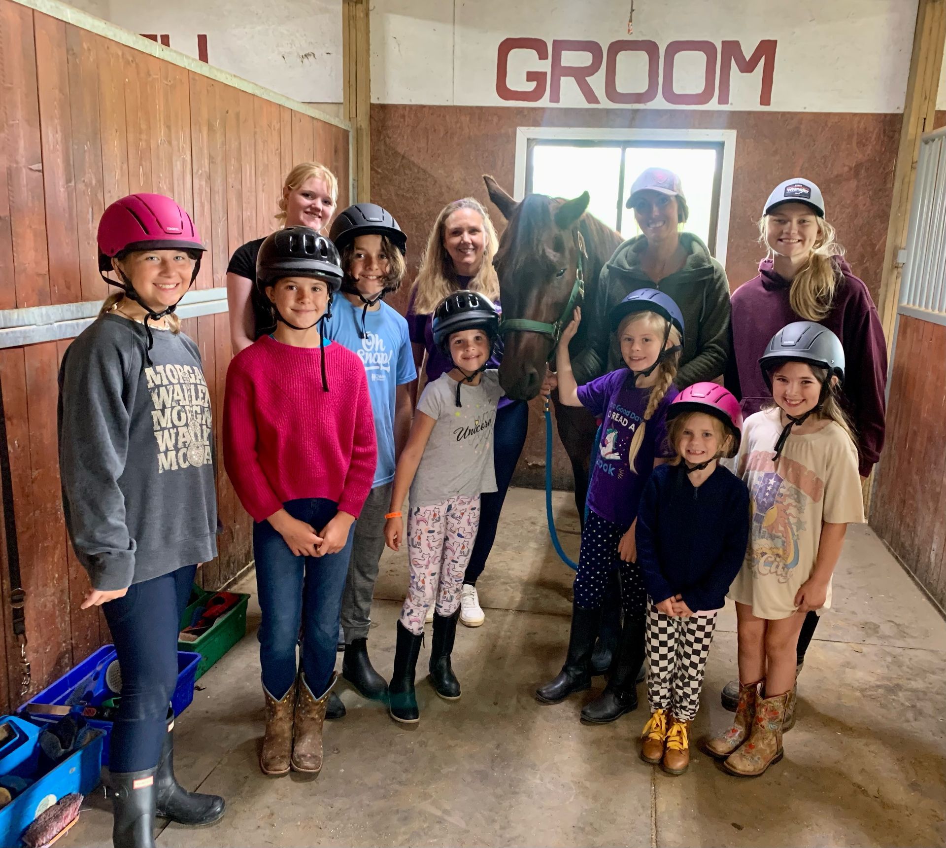 Group of children in riding helmets with a horse in a stable; 