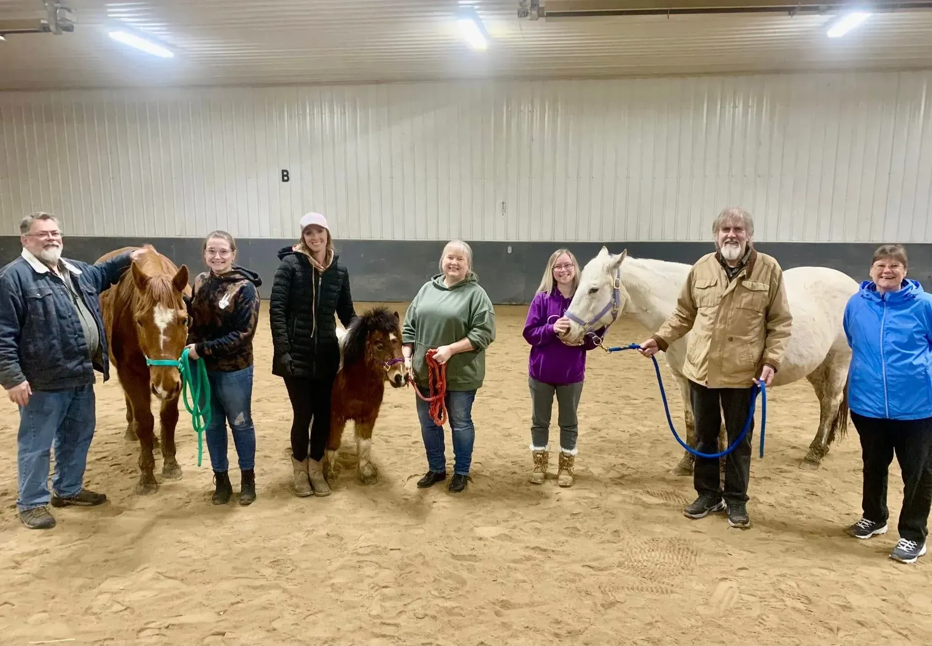 Group of people with horses in an indoor arena; they are smiling.