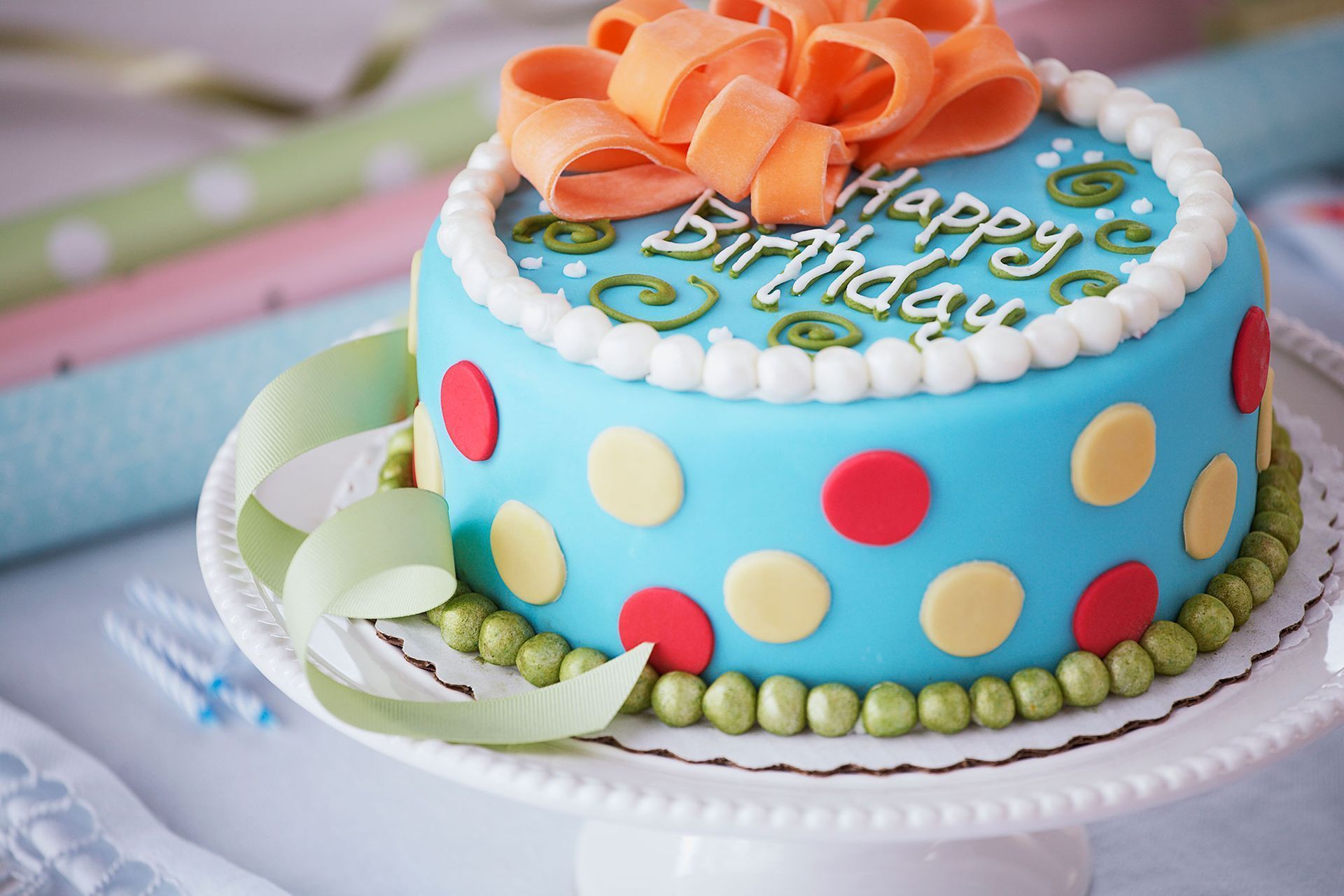 Birthday cake with blue frosting, polka dots, and an orange bow.