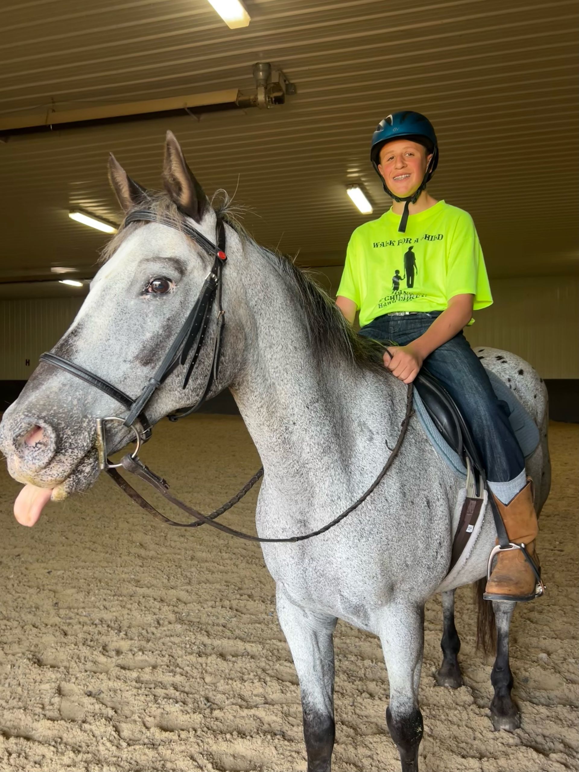 A person in a helmet and neon green shirt rides a gray horse in a riding arena.
