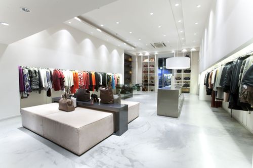 Modern clothing boutique interior with bright white walls, marble floor, and colorful garments on display racks.