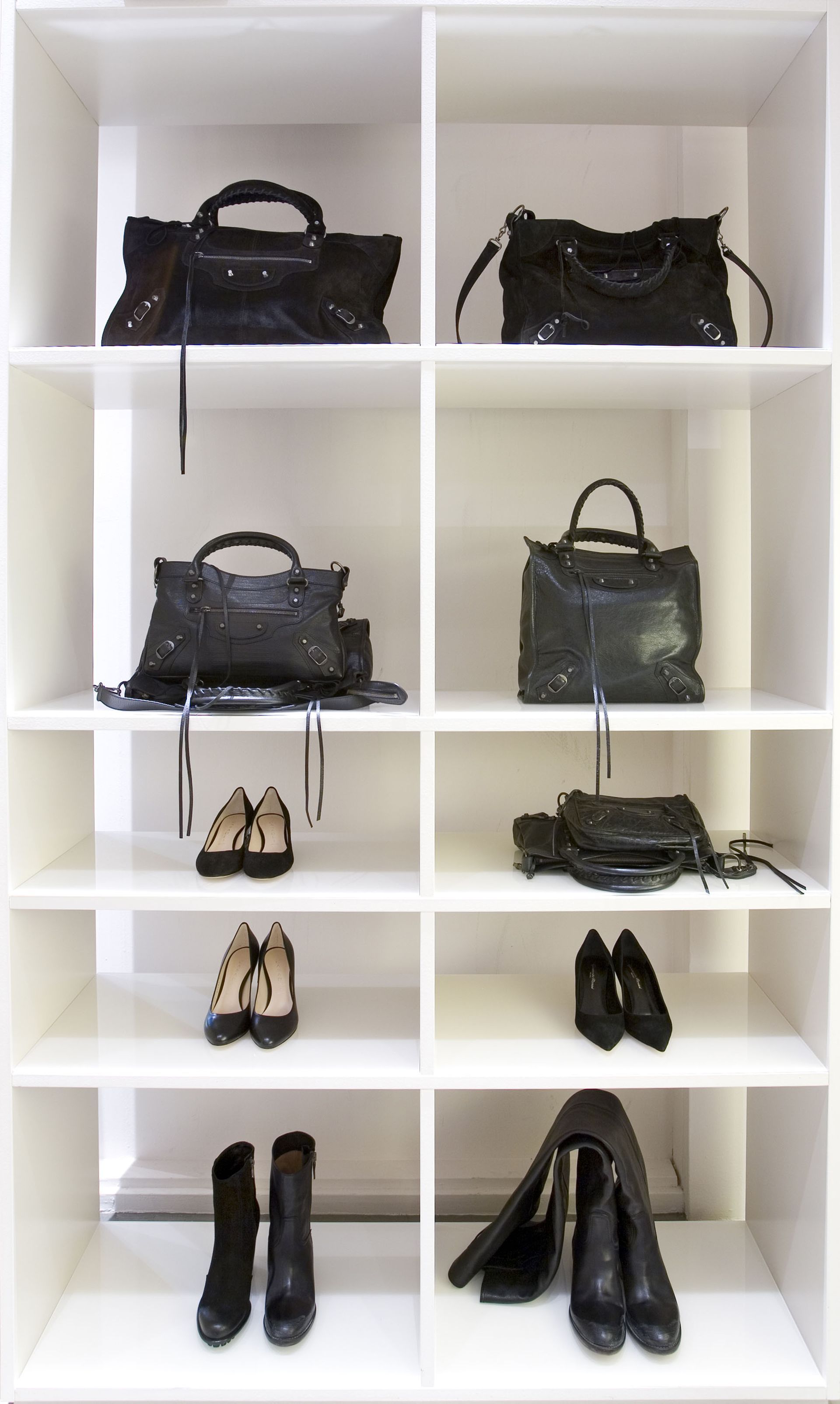 White cubby shelves displaying black handbags, small heels, and black boots