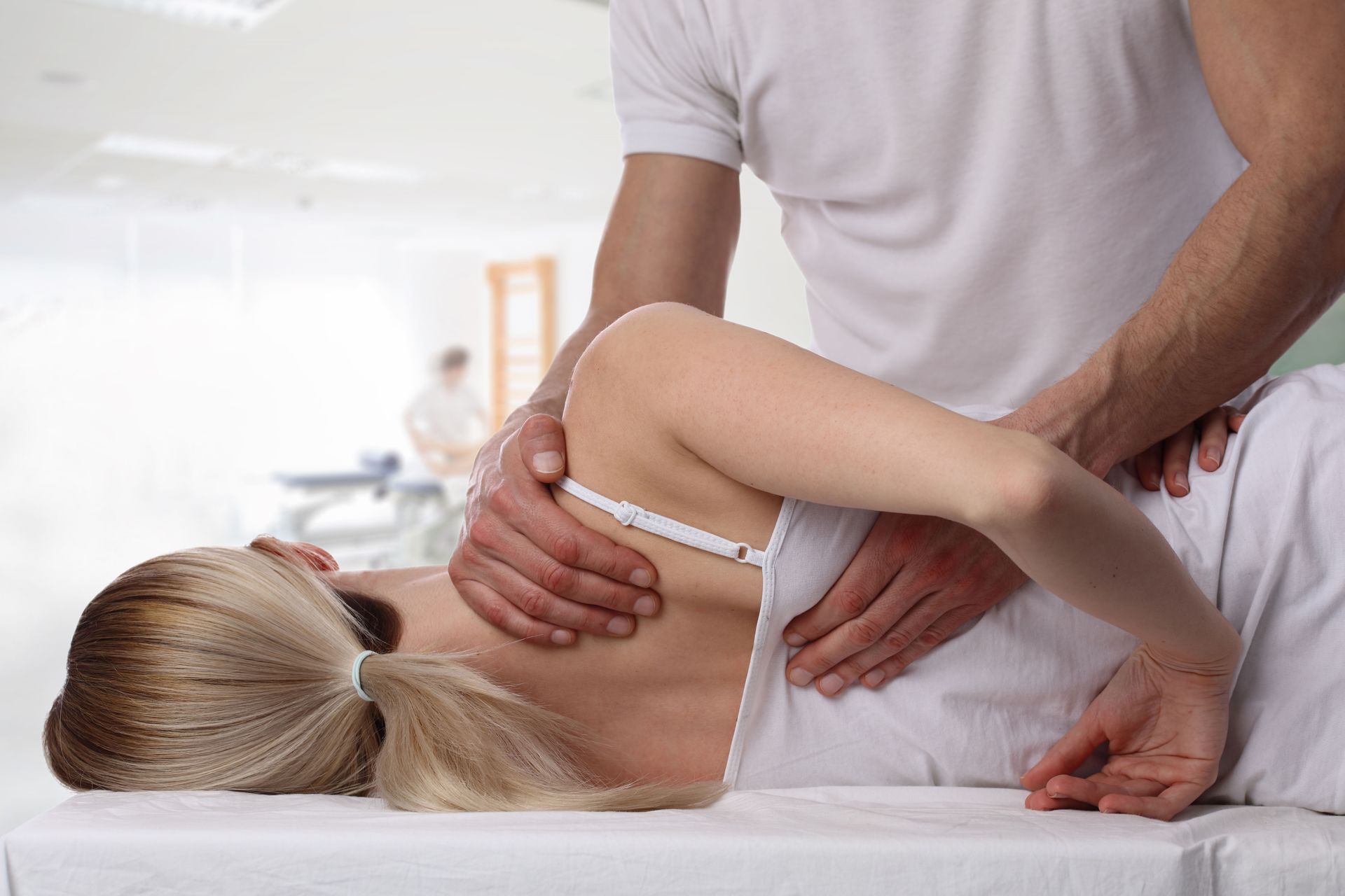 Massage therapist adjusting a woman&rsquo;s shoulder during a treatment on a table