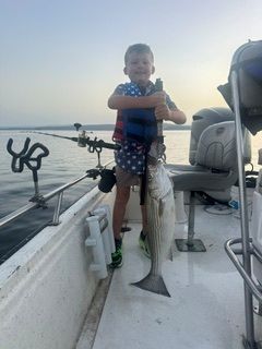 Child holding a large fish on a boat deck at sunset