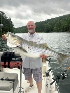 Man holding a large striped bass on a boat on a cloudy lake