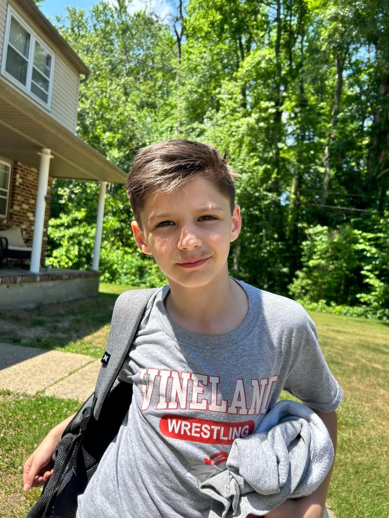 A young boy wearing a grey t-shirt is standing in front of a house.