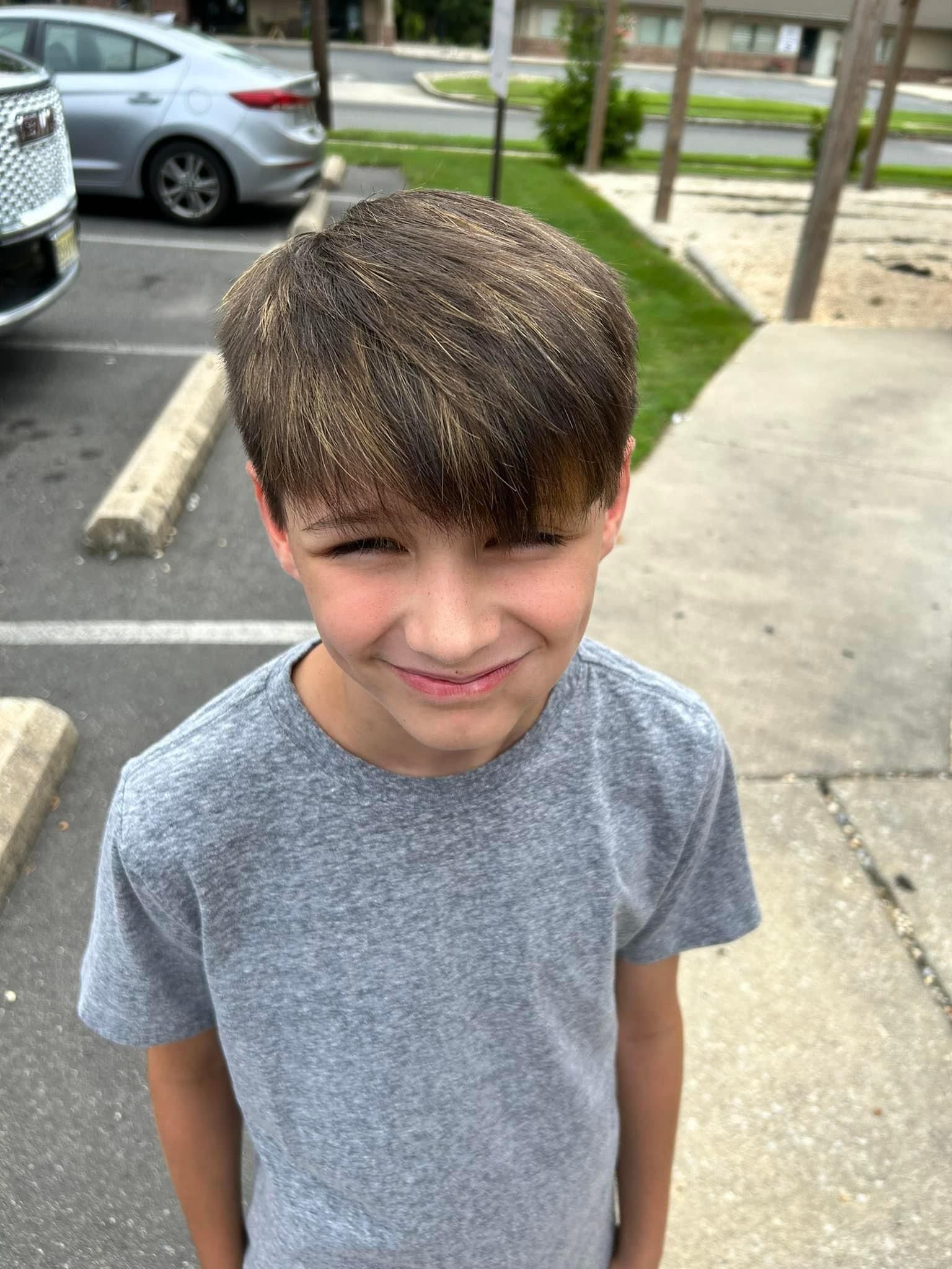 A young boy wearing a grey t-shirt is standing in a parking lot.