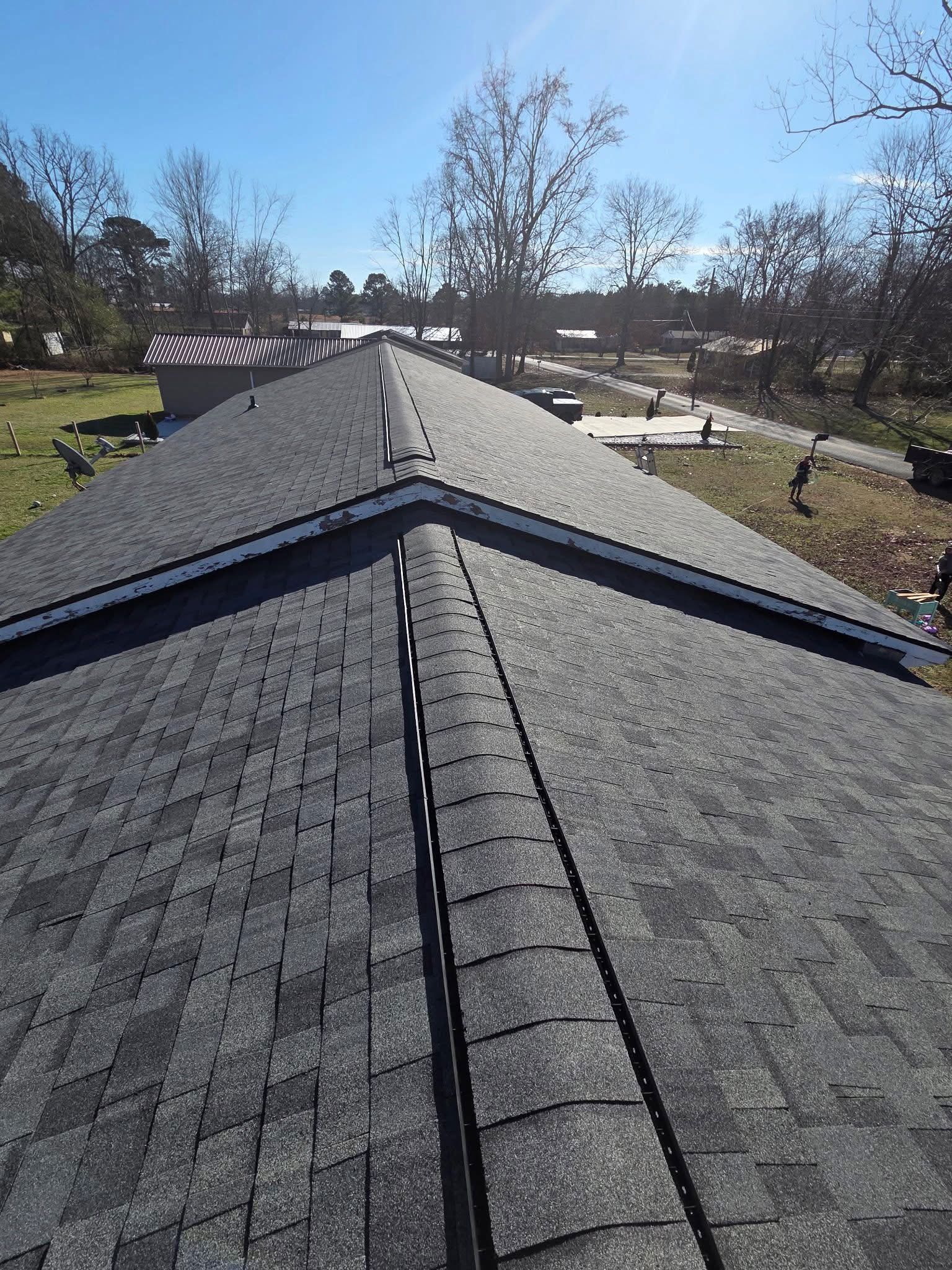 A high-angle view looking down the peak of a dark-shingled residential roof on a sunny day.