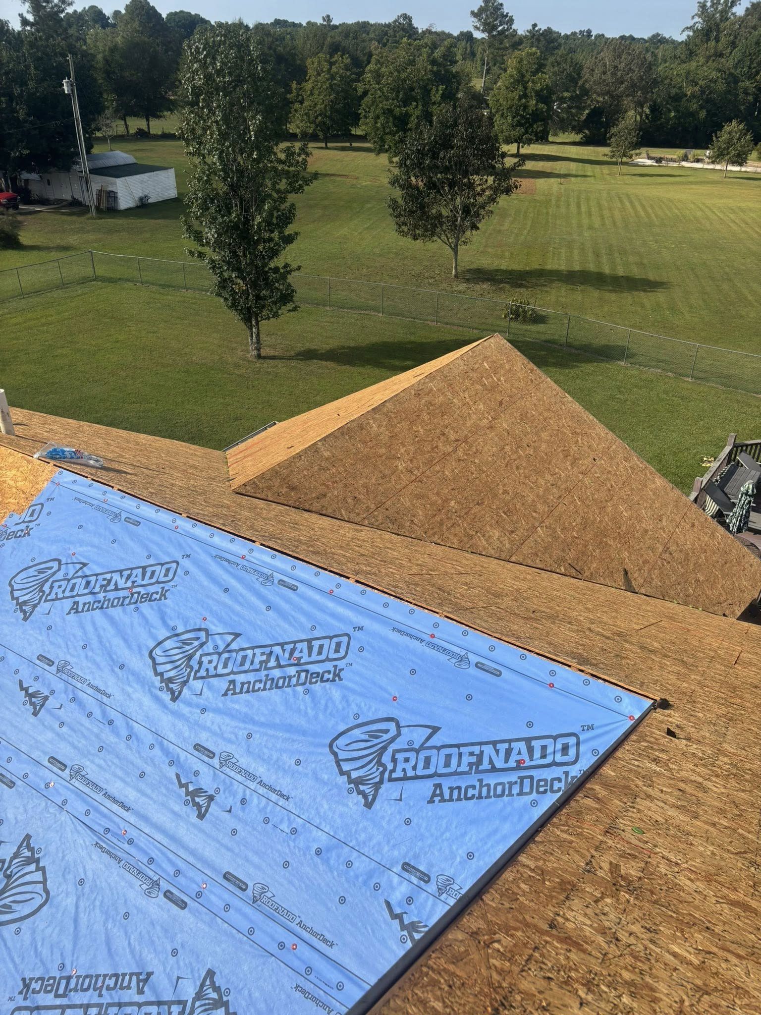 A partially shingled roof under construction with blue synthetic underlayment covering one section of the wooden deck.