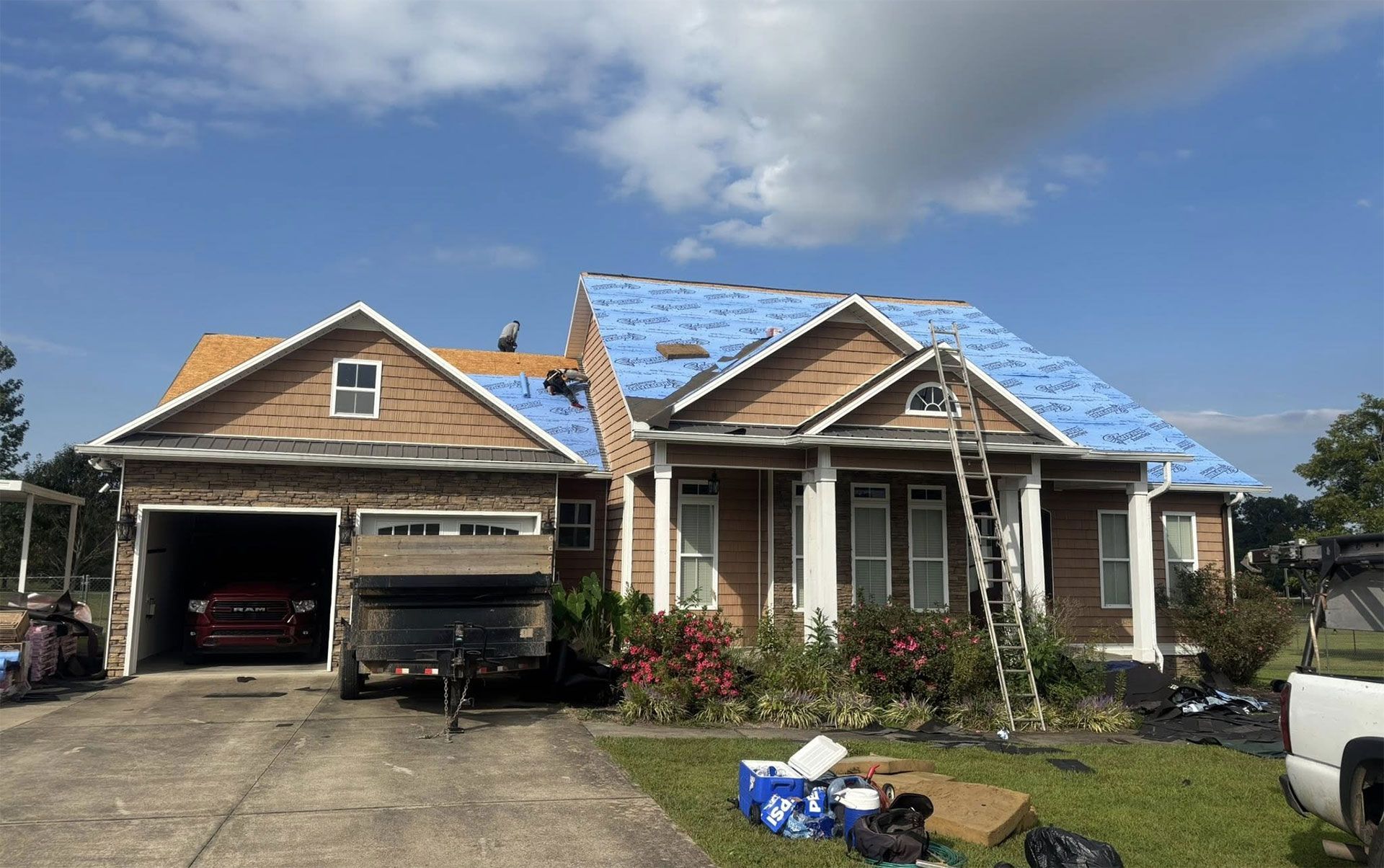 A house with a partially replaced blue underlayment roof, a ladder leaning against the front, and a car in the garage.