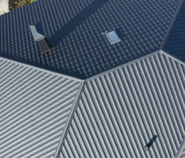 Gray and black metal roof with a chimney and small window.