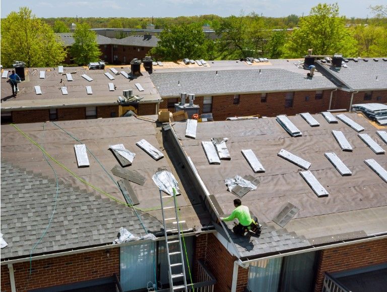 Roofers working on a building, partially tearing off old shingles and installing new ones; sunny day.