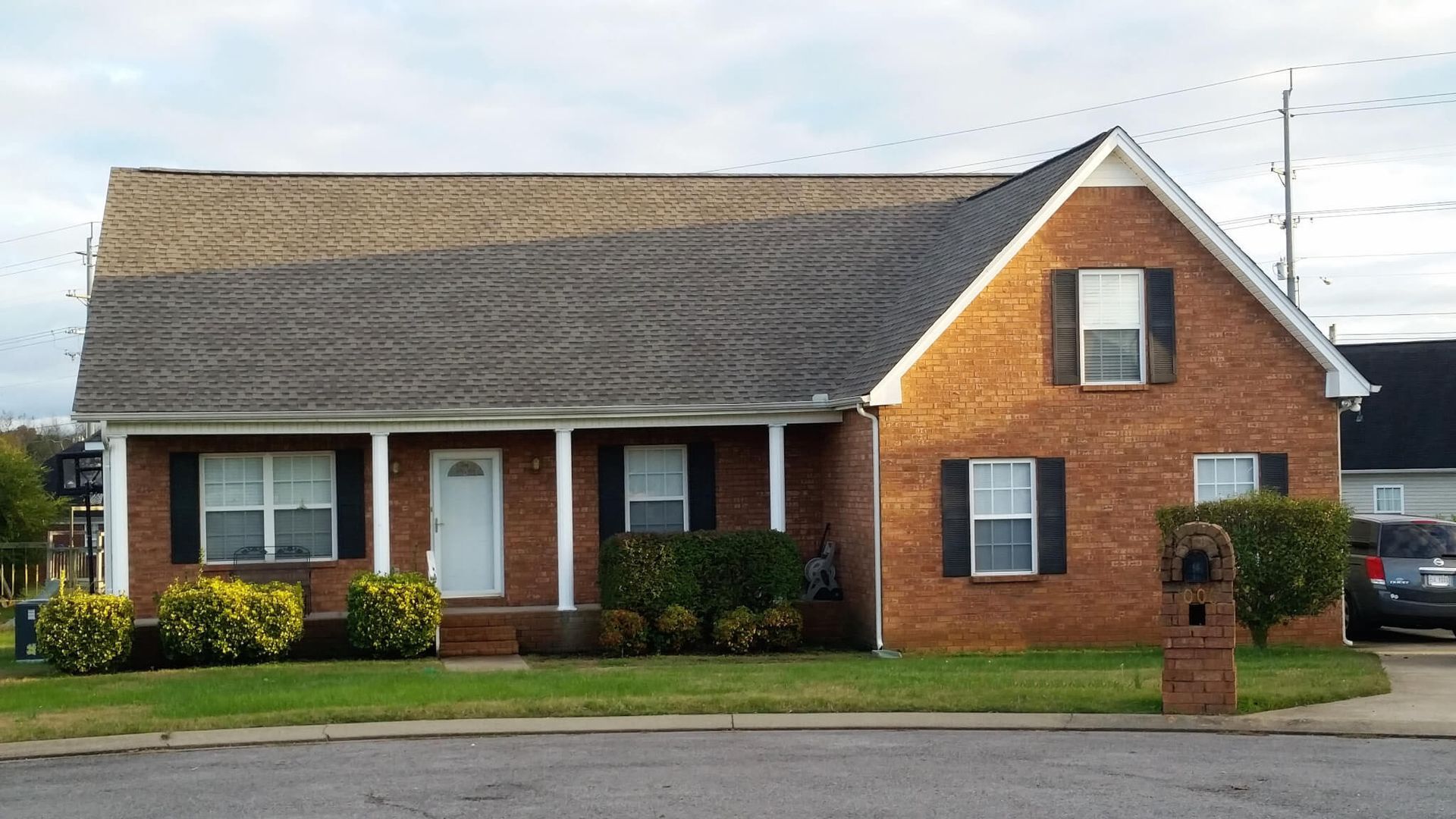 Brick house with black shutters, white door, and green lawn.