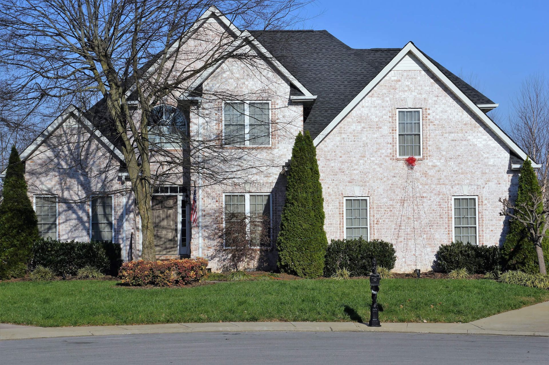 Two-story brick house with dark roof and green lawn, under a bright blue sky.