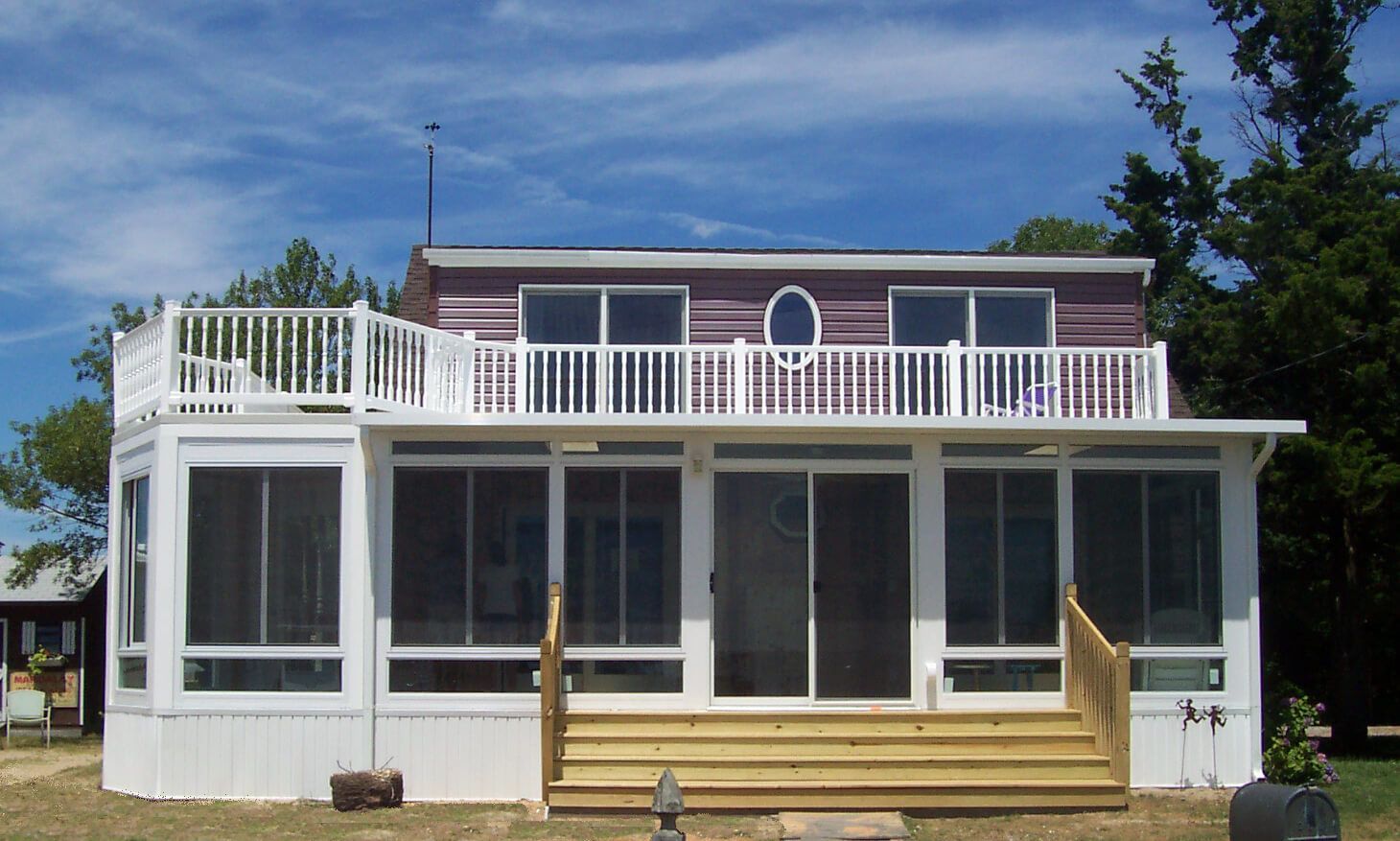 Two-story house with a screened-in porch and deck, blue sky, white trim, and a wooden staircase.