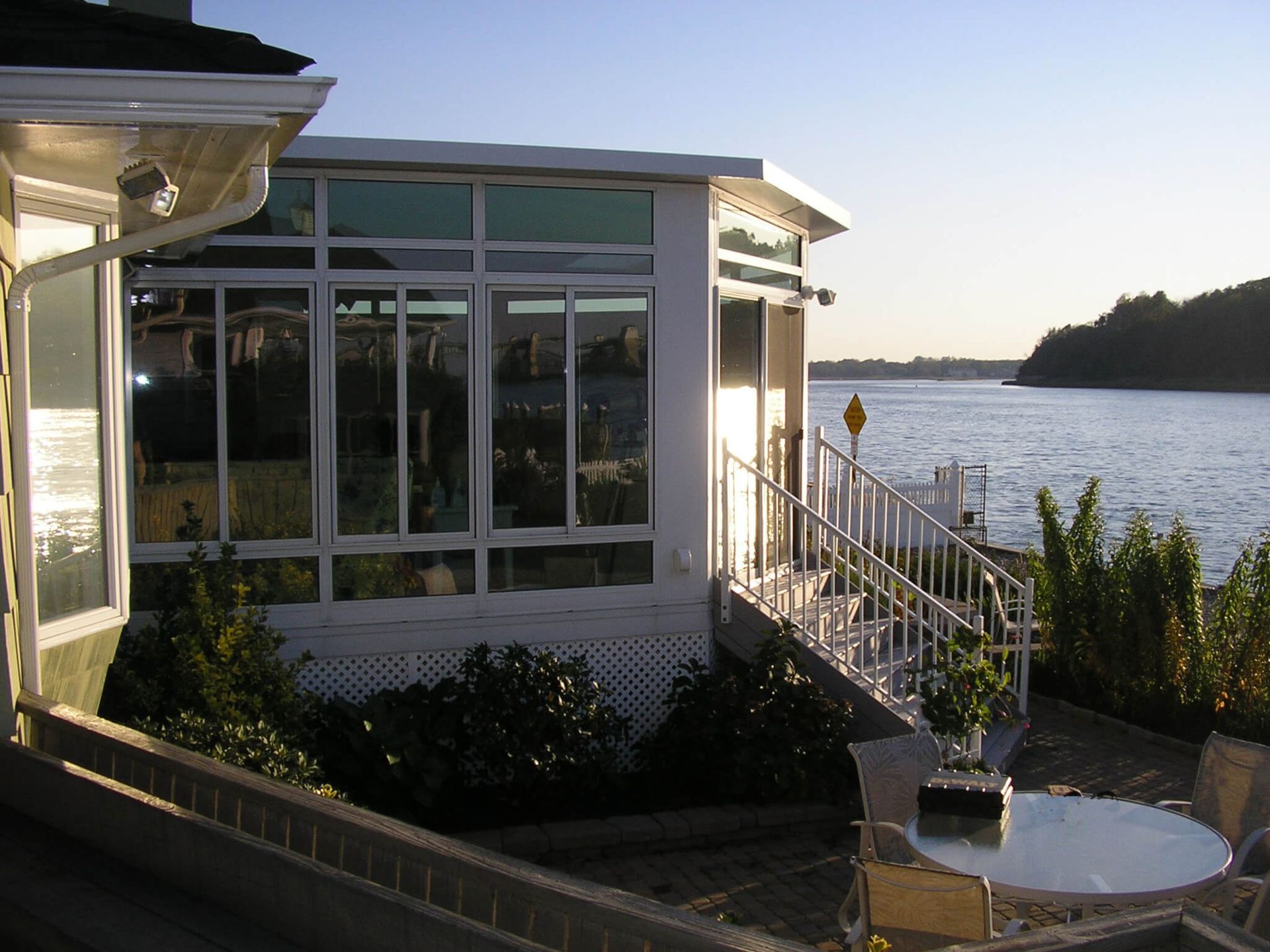 Waterfront home with white framed windows, deck, and stairs leading to a dock.
