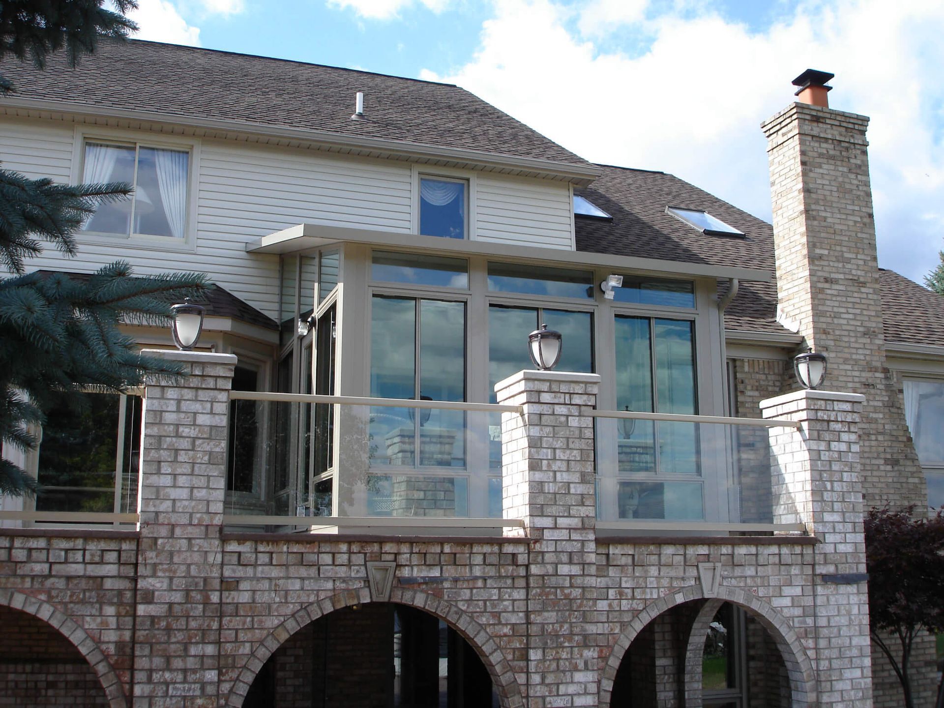 Back of a house with a brick deck and a sunroom with large windows, under a blue sky.