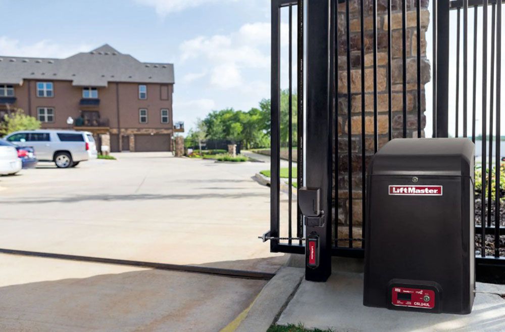 Driveway gate with black security box and keypad beside a brick apartment building.