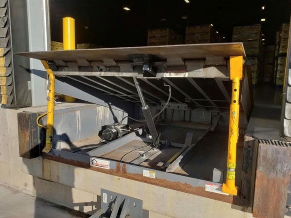 Industrial scissor lift platform loading dock, lowered with yellow safety posts in a warehouse bay
